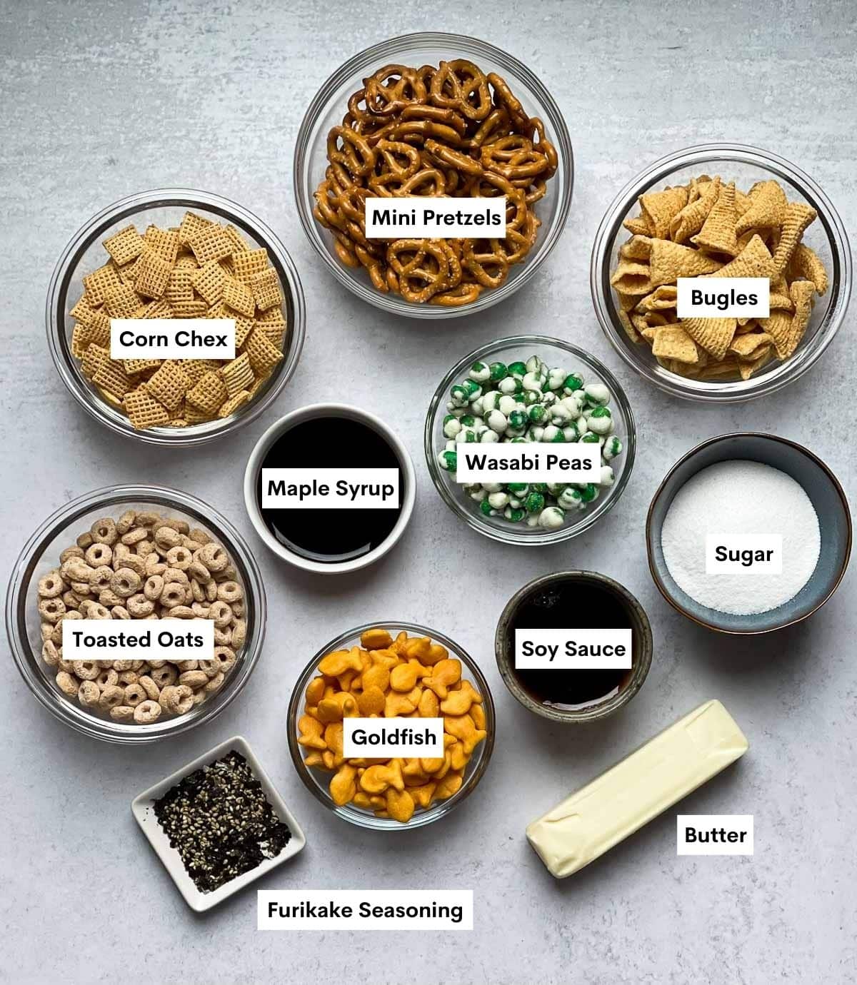 Labeled ingredients in bowls for Furikake Chex Mix Snack recipe on top of a gray surface.