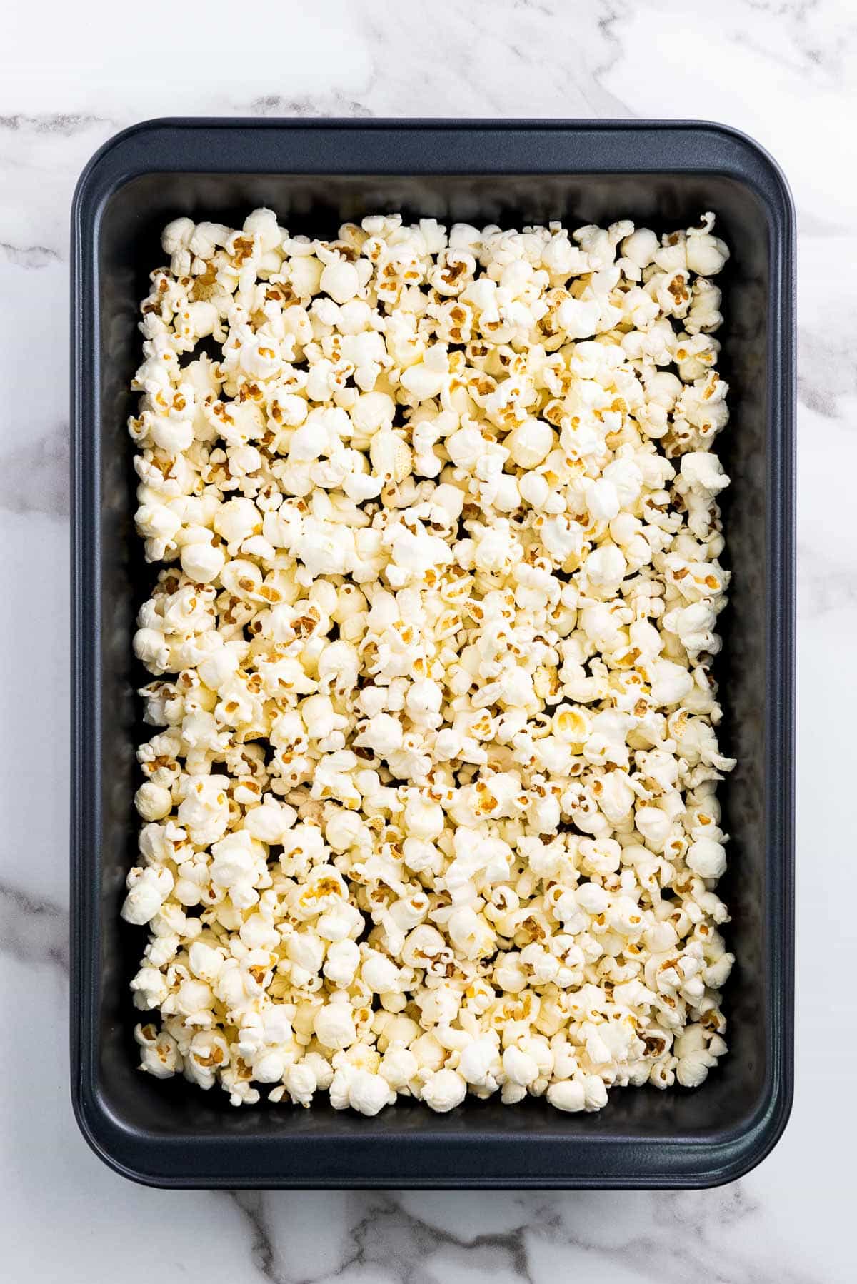 Popcorn in a black baking tray on top of a marble surface.