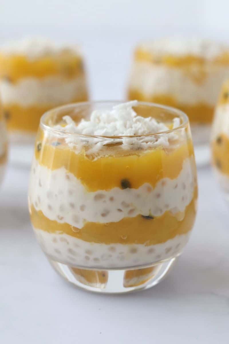 Coconut mango tapioca pudding layered in a glass dessert cup with other puddings in the background.
