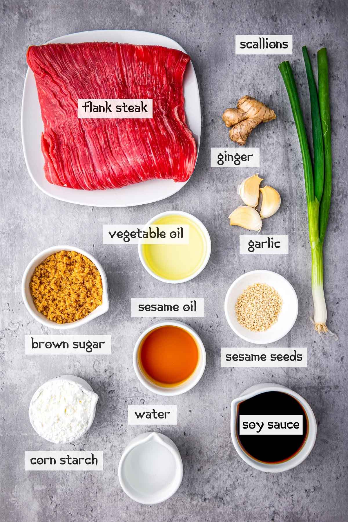 Labeled ingredients for making Slow Cooker Mongolian Beef in small bowls on top of a gray surface.