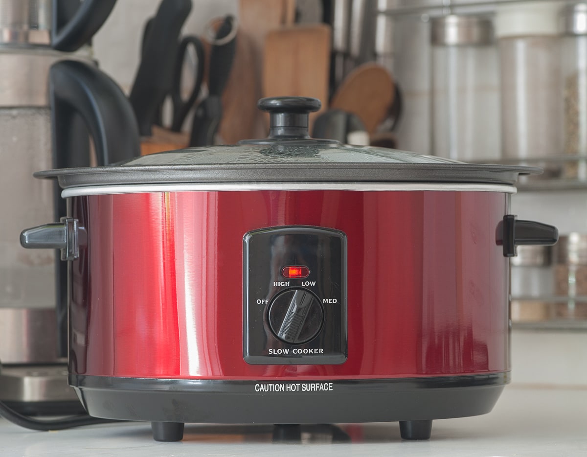 Close up of a red slow cooker working on top of a kitchen counter