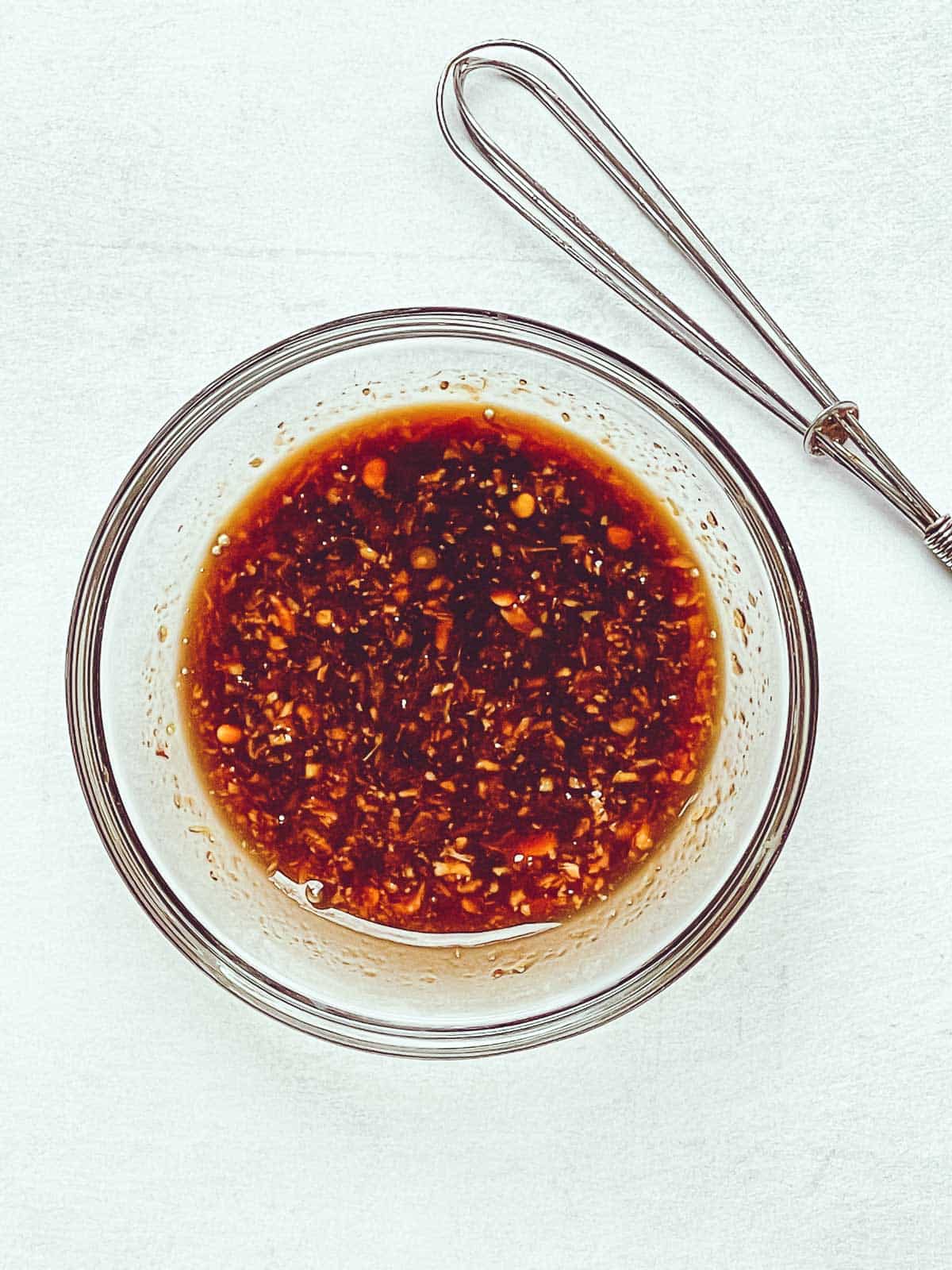 A spicy red chili sauce in a glass bowl with a small whisk on the side.
