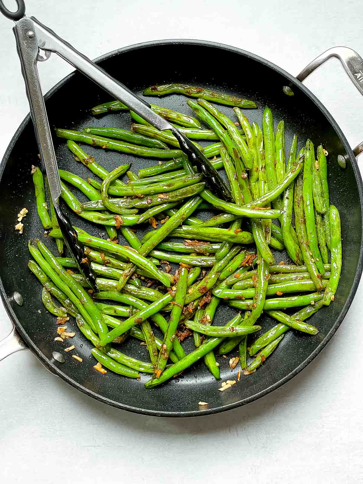 Chinese Garlic Green Beans sauteed in a frying pan with tongs inserted.