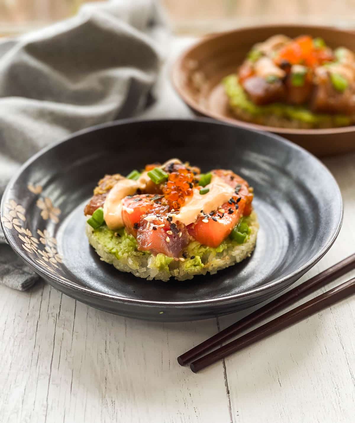 Sushi waffles with salmon and tuna on two round plates with a side of chopsticks on top of a white surface with a napkin in the background.