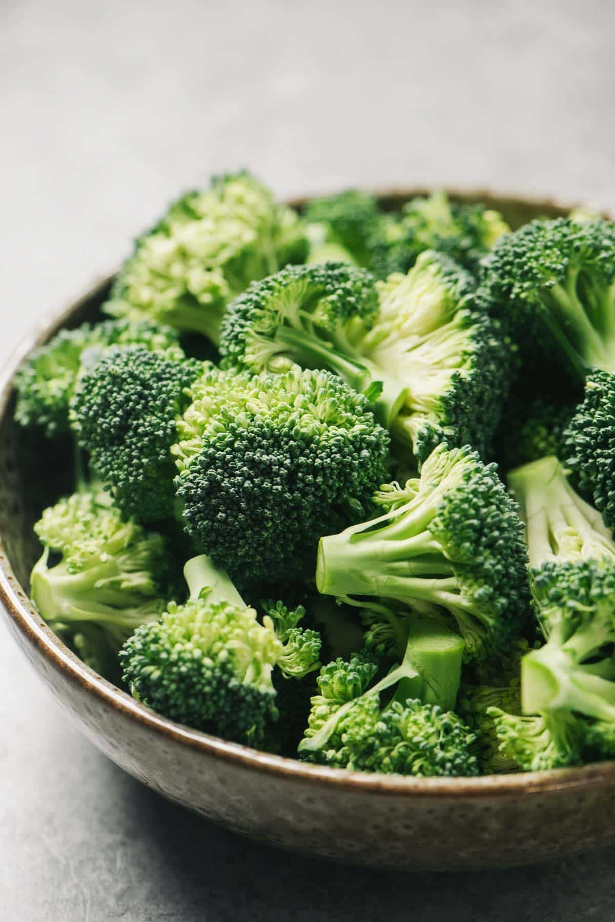 Broccoli florets in a white bowl on top of a white surface.