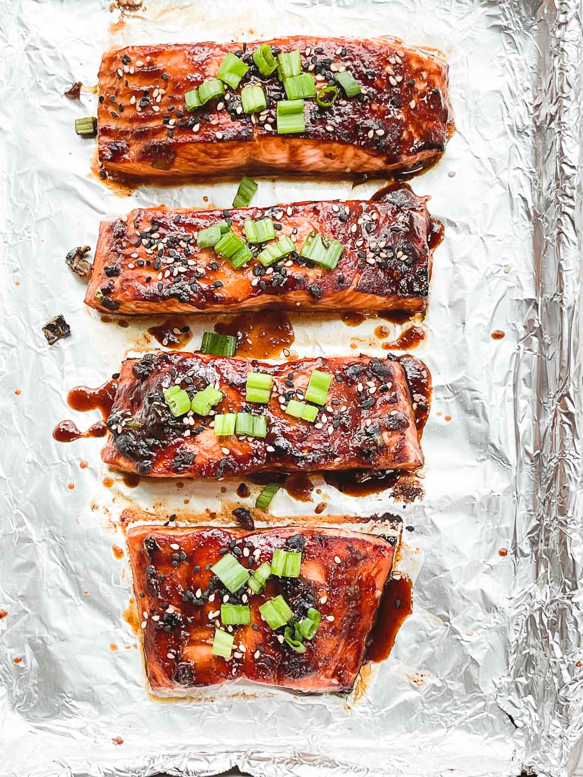 Broiled miso glazed salmon filets topped with chopped green onions on a baking sheet lined with tin foil.