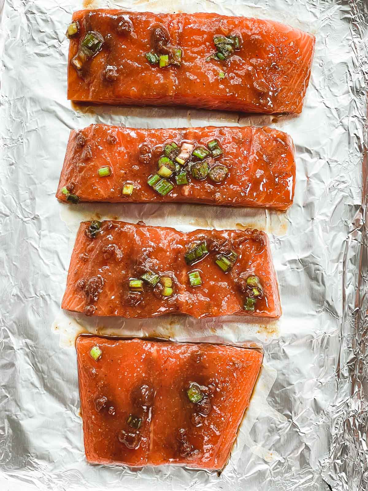Four salmon filets topped with a miso marinade on a baking tray lined with tin foil ready for the oven.