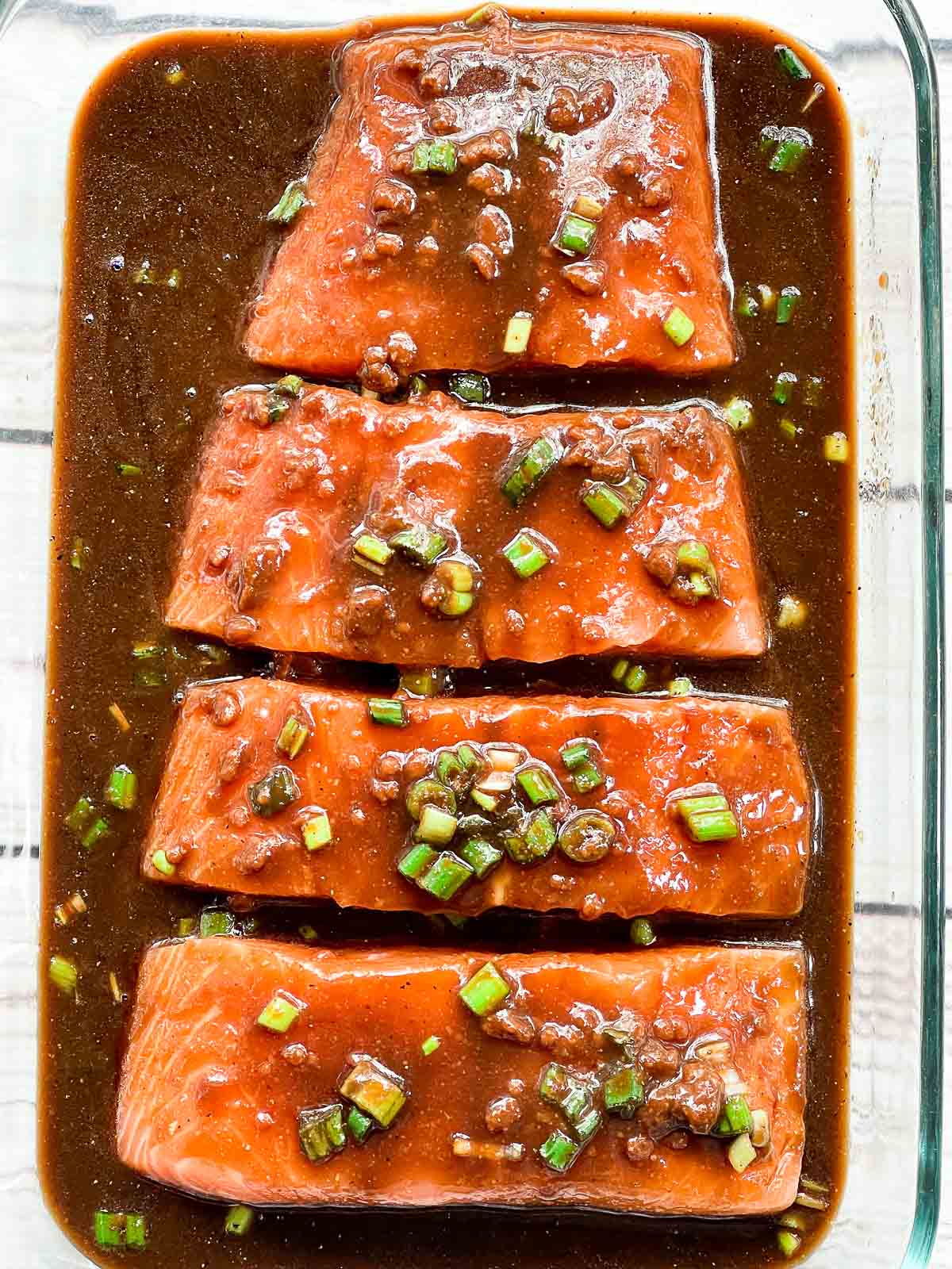 Four raw salmon filets marinating in a glass pyrex dish.