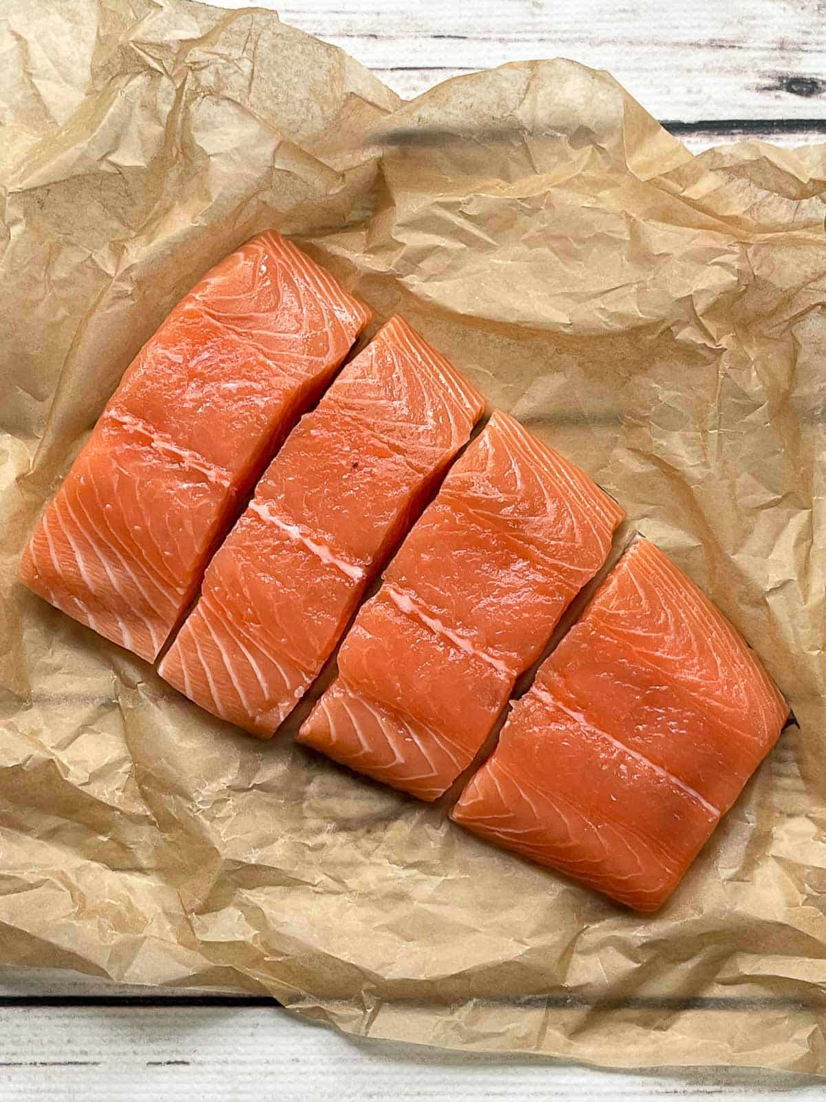 Raw salmon filets on brown parchment paper on top of a white board.