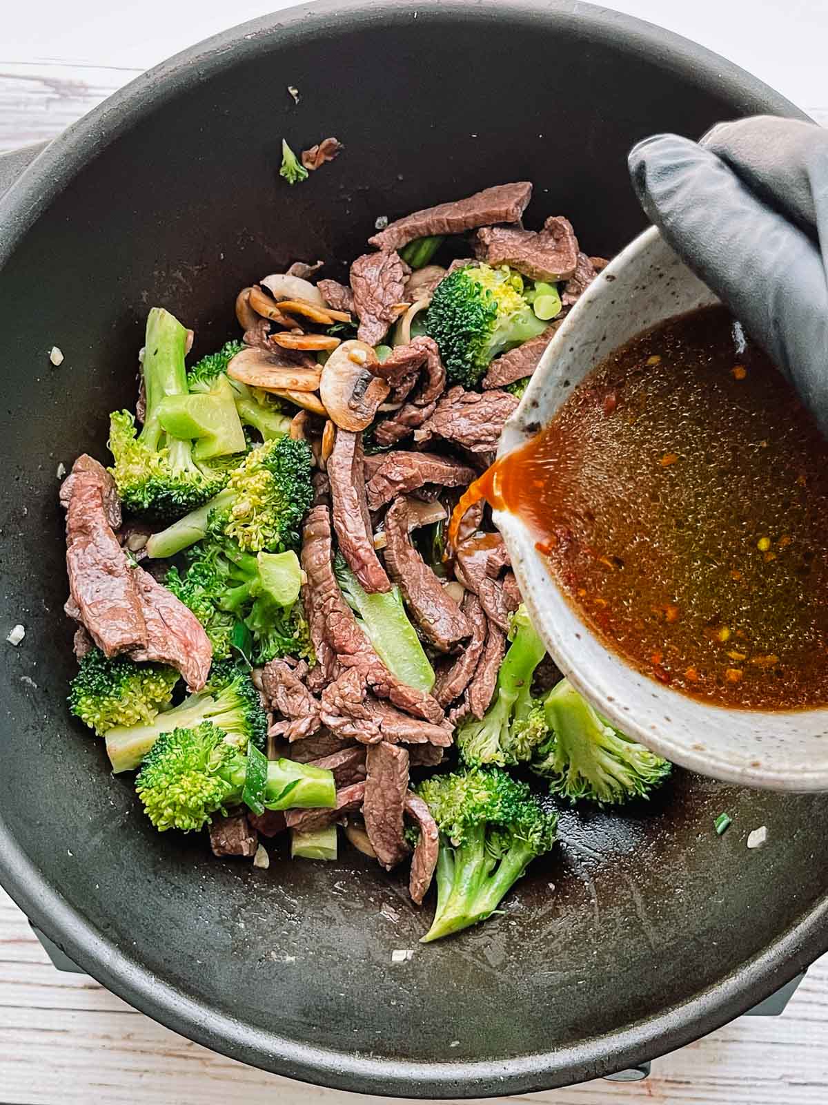 Pouring the sauce over beef and broccoli stir fry in a large wok.