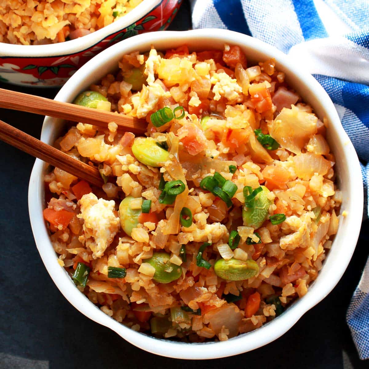 Cauliflower Kimchi Fried Rice in a white bowl with wooden chopsticks and a blue and white napkin on the side.