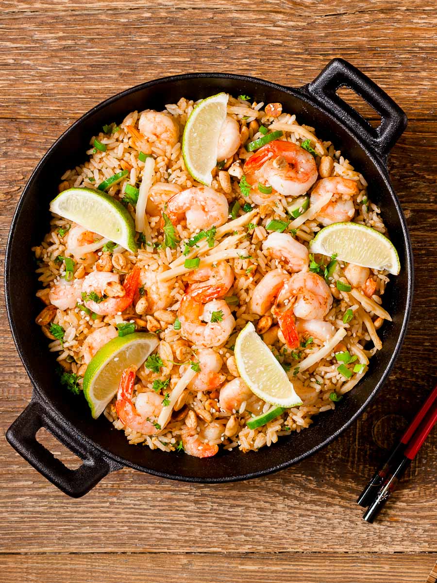 Shrimp Fried Rice with lime wedges on top in a black cast iron pan on top of a wooden board.