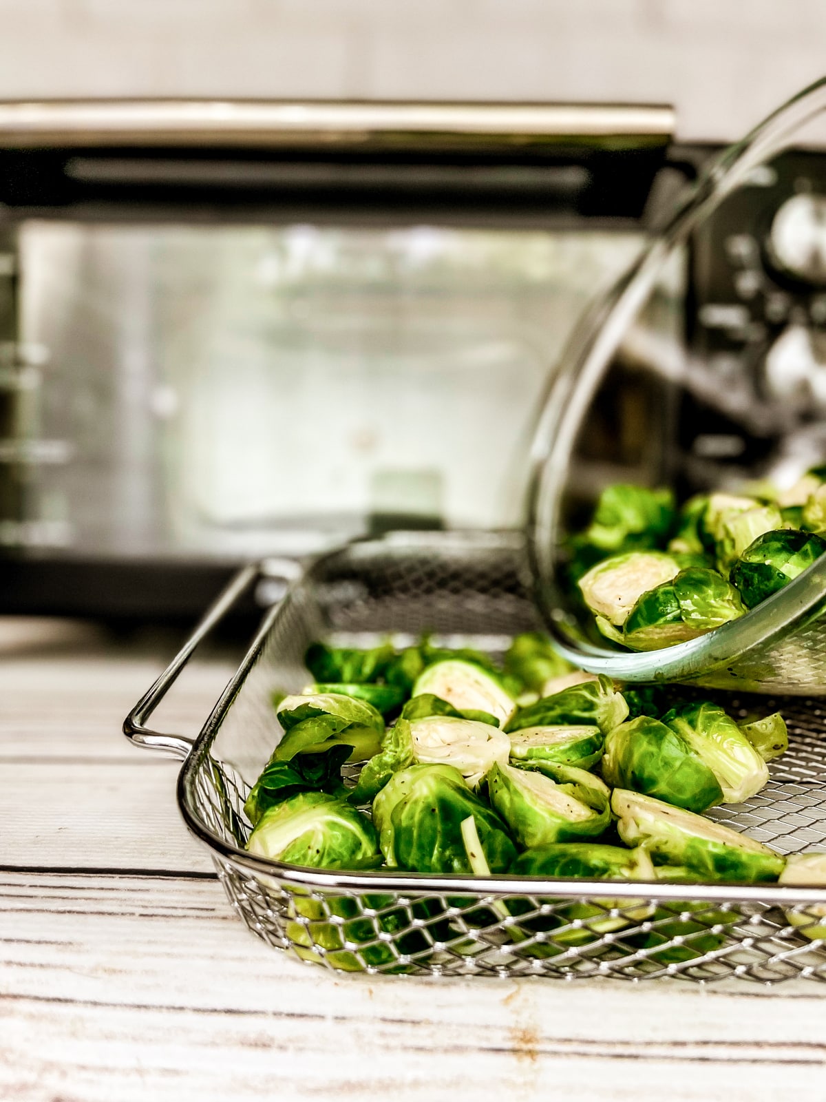 Raw, sliced brussels sprouts being poured into an air fryer basket ready to be cooked.
