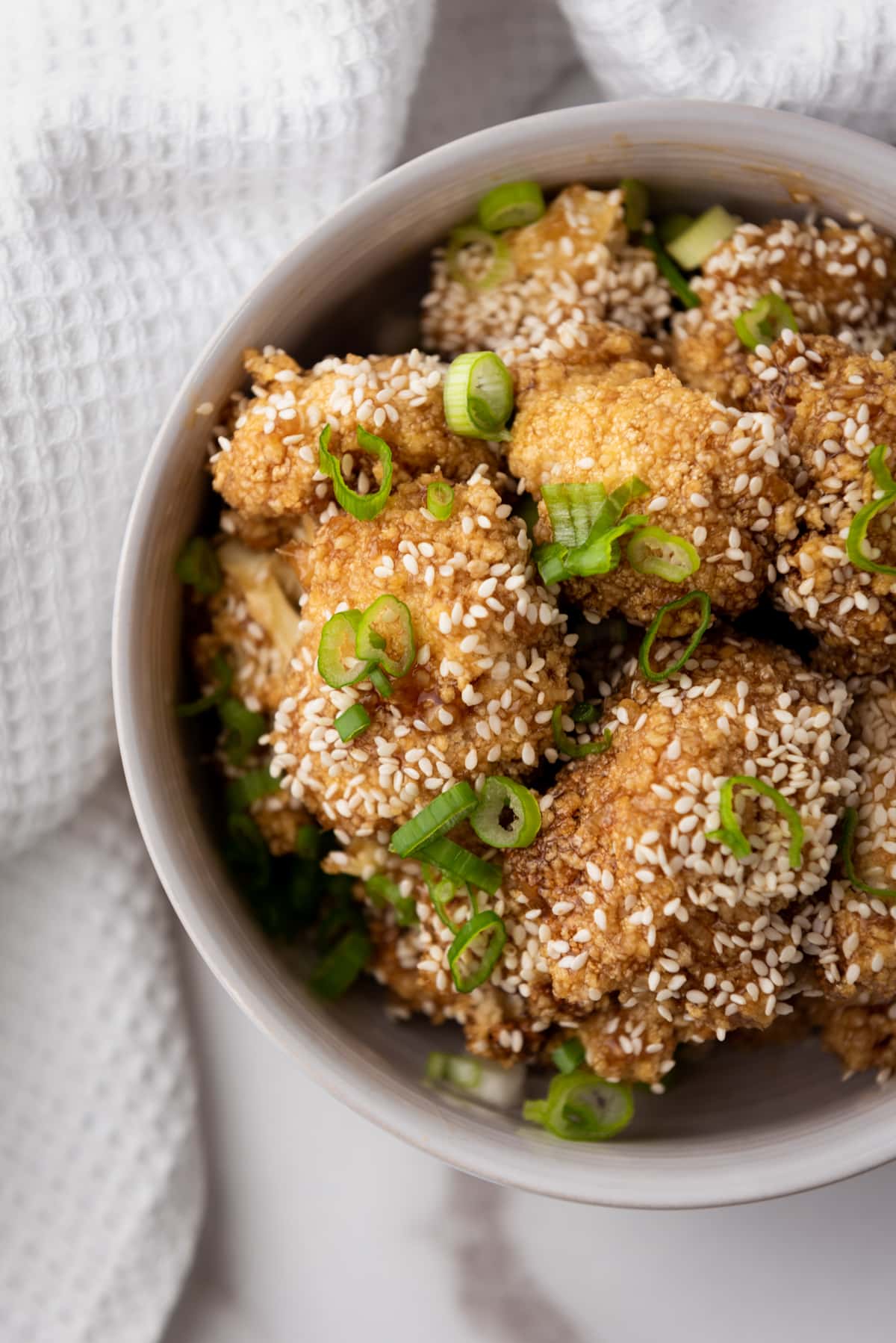 Air Fryer Teriyaki Cauliflower Wings topped with sesame seeds and sliced scallions in a white bowl on top of a marble surface with a white napkin.