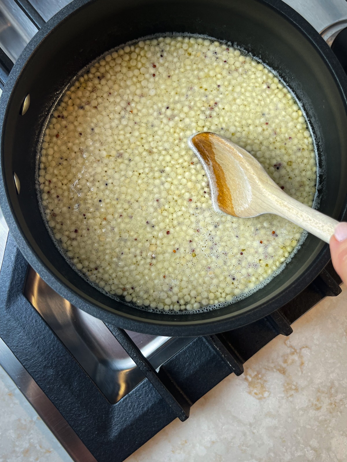 A wooden spoon stirring couscous in a pot over a stove.